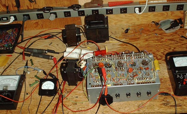 Photo showing workbench with transformers, power resistors, meters, and the breadboard scattered across it.
