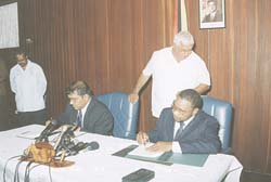 President Bharrat Jagdeo (seated at left) and Opposition Leader, Mr. Robert Corbin (right) signing the Joint Communique in the Credentials Room of the Presidential Secretariat.    Standing at left is Presidential Advisor, Mr. Kellowan Lall and in background Mr. Vic Persaud, Chief of Protocol, Office of the President.