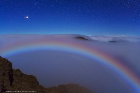 Mars and a Colorful Lunar Fog Bow  Credit & Copyright: Wally Pacholka (AstroPics.com, TWAN)  Explanation: Even from the top of a volcanic crater, this vista was unusual. For one reason, Mars was dazzlingly bright two weeks ago, when this picture was taken, as it was nearing its brightest time of the entire year. Mars, on the far upper left, is the brightest object in the above picture. The brightness of the red planet peaked last week near when Mars reached opposition, the time when Earth and Mars are closest together in their orbits. Arching across the lower part of the image is a rare lunar fog bow. Unlike a more commonly seen rainbow, which is created by sunlight reflected prismatically by falling rain, this fog bow was created by moonlight reflected by the small water drops that compose fog. Although most fog bows appear white, all of the colors of the rainbow were somehow visible here. The above image was taken from high atop Haleakala, a huge volcano in Hawaii, USA.