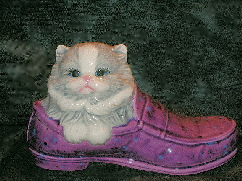 A gray/white glazed, ceramic cat in a purple-multicolor glazed, loafer shoe.