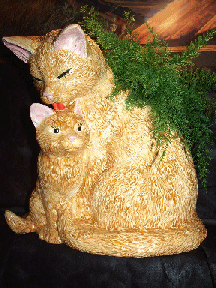A yellow glazed, ceramic mama/baby cat with air fern.