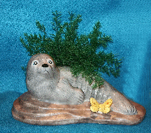 A gray glazed, ceramic seal, with air fern, on a beige rock