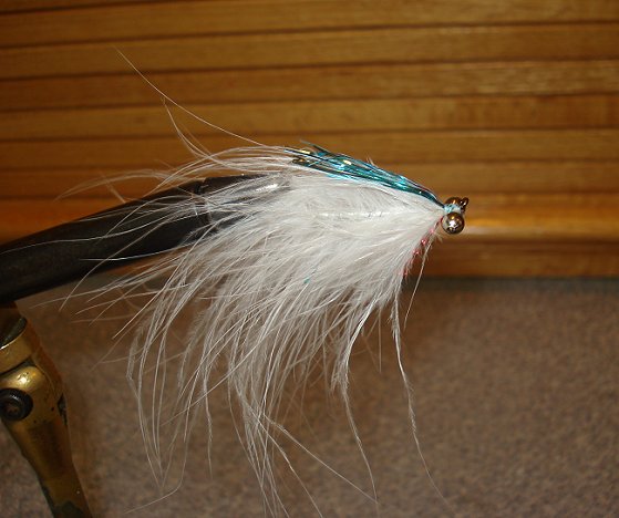 Rotate fly over in vice and tie in 12 strands of sky blue flashabou behind the eyes. Careful not extend blue flashabou beyond the hook point. If the material fouls, the action of the fly is ruined.