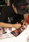 After autographing a signboard from GADGUARD (where he's the mecha designer), Murata-san grumpily signs a copy of the soundtrack cover for HELLSING, a hugely successful anime title (but one which he secretly hates creating the character designs for)!