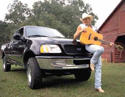 Alan leaning on black truck holding his guitar