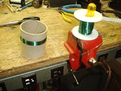 Partially wound coil sitting on work bench with slack wire visible running between the spool and the coil form.